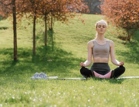 Woman practicing meditation in a sunny park, enhancing wellness and mindfulness.