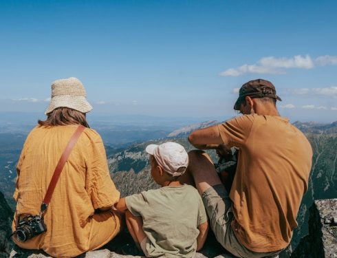 Family sitting on a rock, enjoying a panoramic view of the Tatra Mountains under clear blue skies.